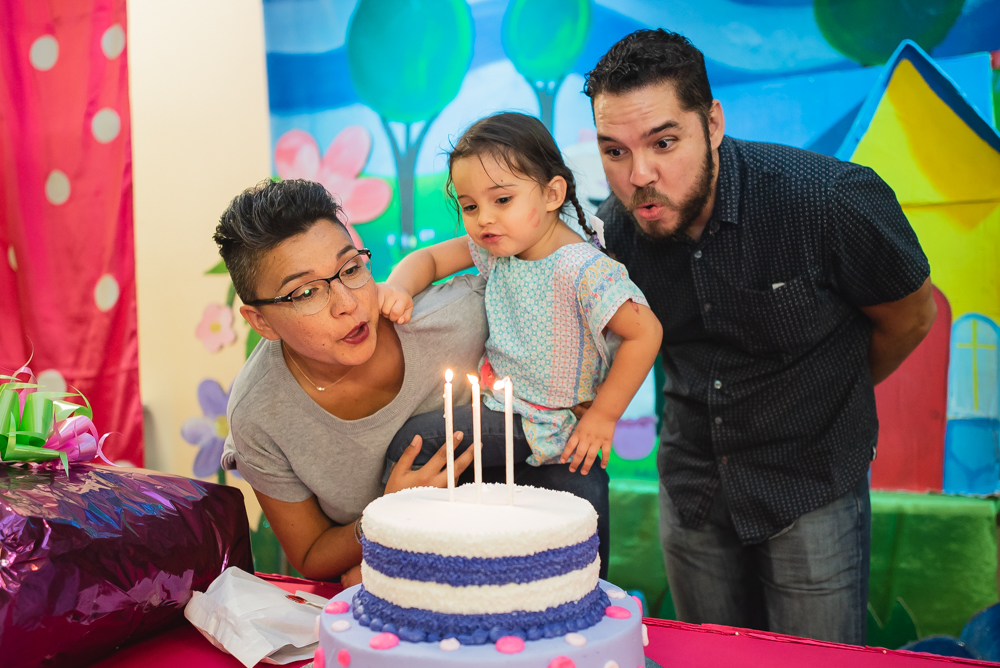 papás ayudando a soplar vela de cumpleaños a niña