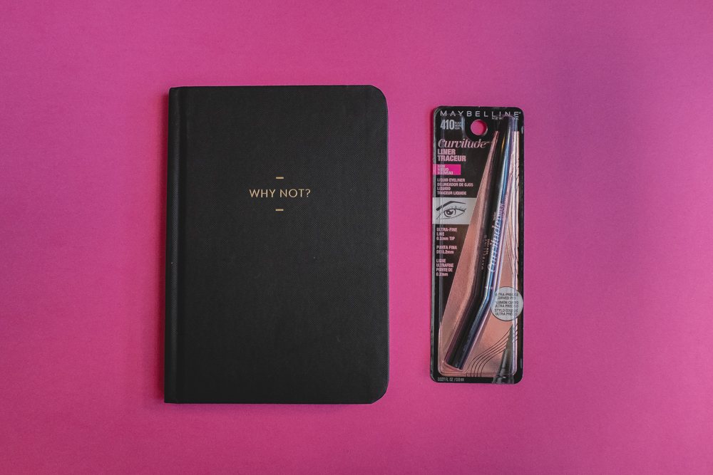 Delineador Curvitude de Maybelline en su empaque sobre fondo rosa a un lado de una libreta