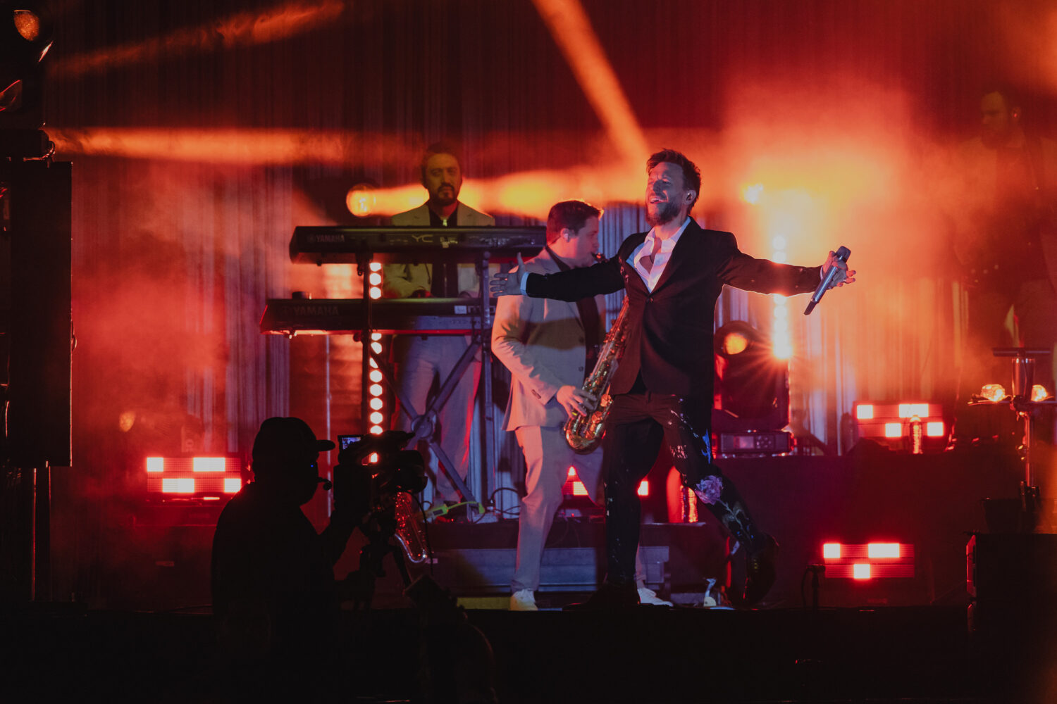 Noel de Sin Bandera durante concierto en Hermosillo. Tiene los brazos abiertos con el micrófono en la mano izquierda.